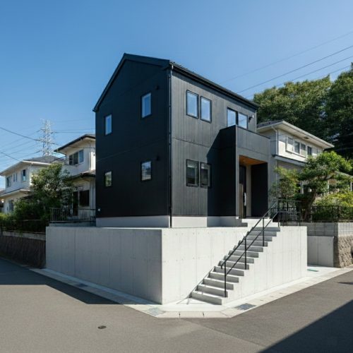コンクリート擁壁の上に建つ、黒いガルバリウム鋼板のモダンな2階建て注文住宅。
