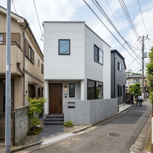 横浜のなだらかな傾斜地に建つ、駐車場1台分を備えたモダンでコンパクトな2階建ての注文住宅の外観